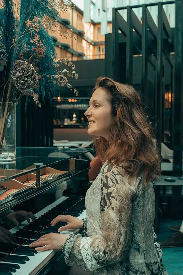 Woman playing piano beside tall flowers and windows