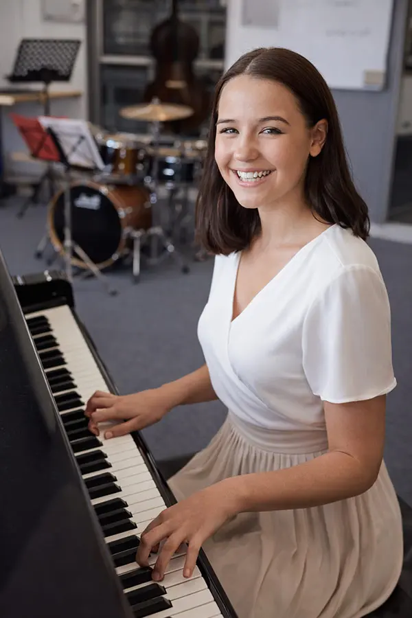 Smiling woman playing piano beside a drum kit