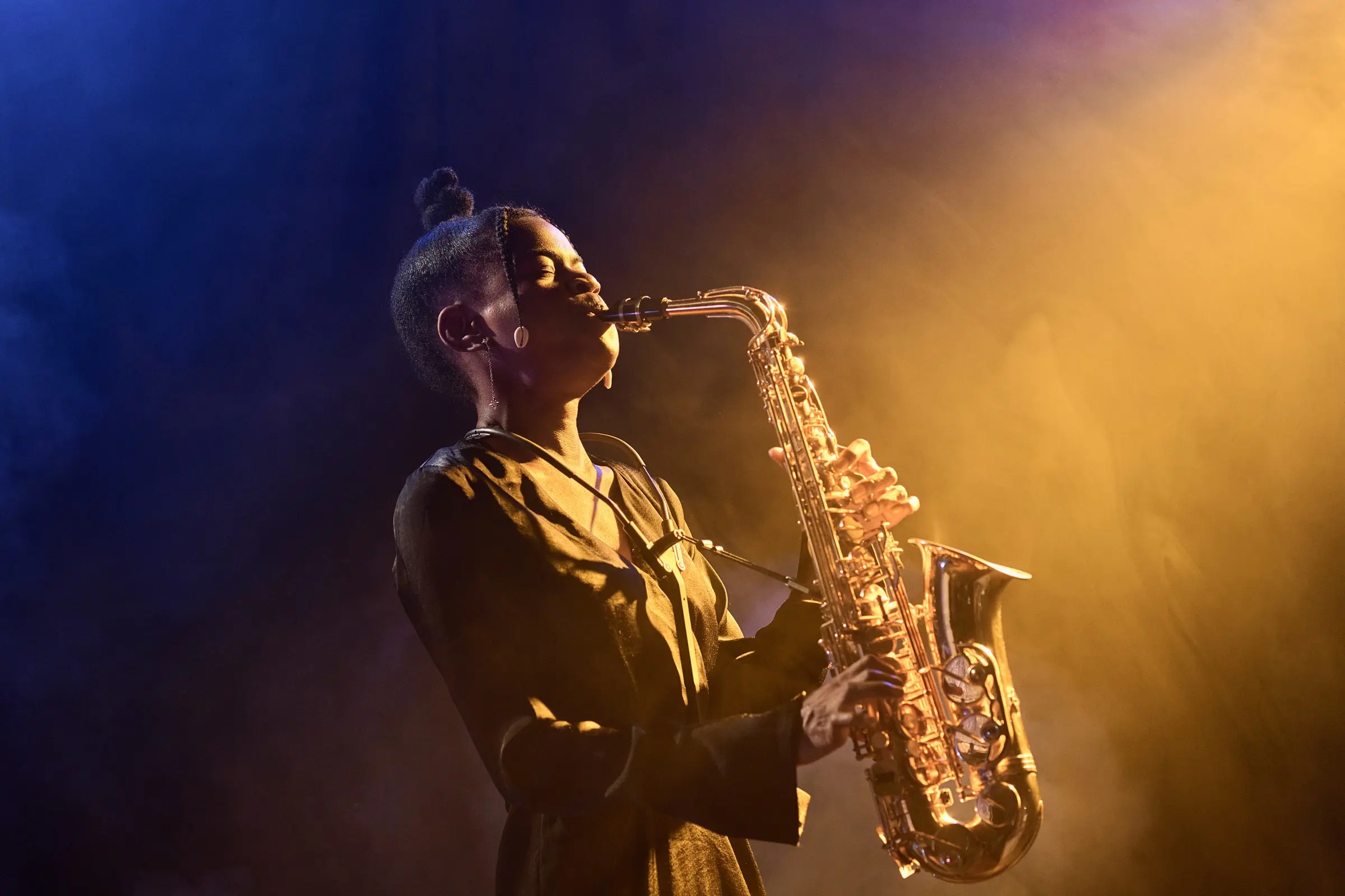 Woman playing the saxophone on stage in warm light.