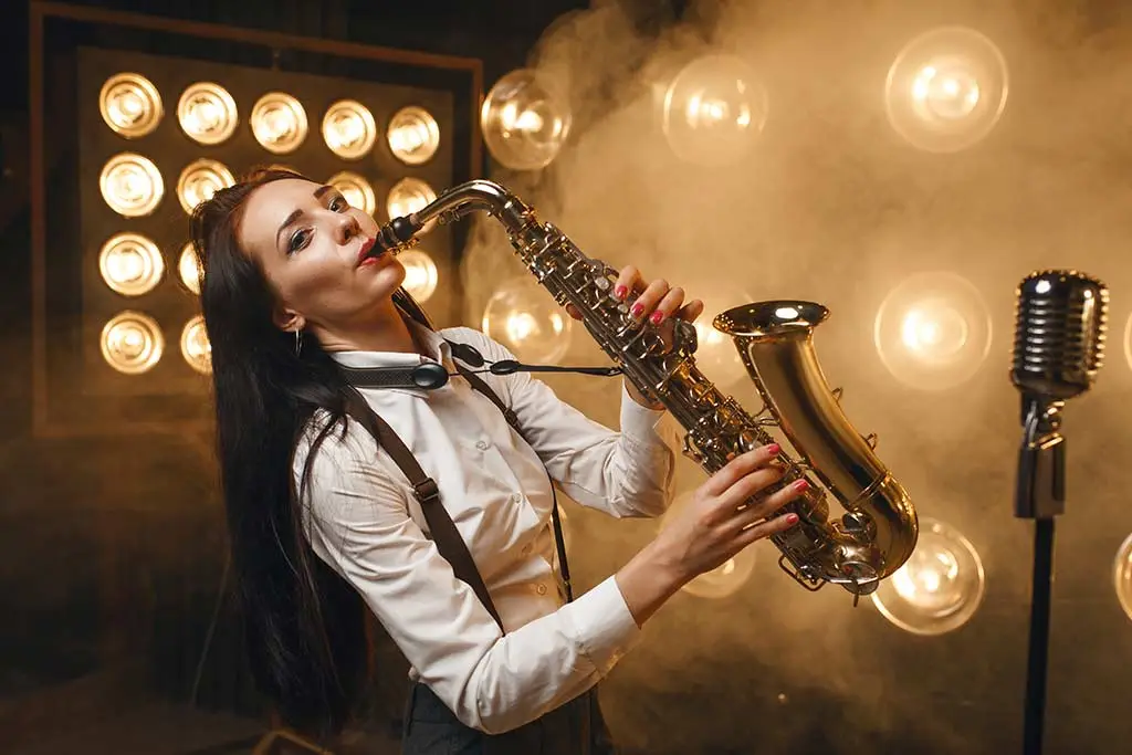 Woman playing saxophone beside a microphone under bright stage lights