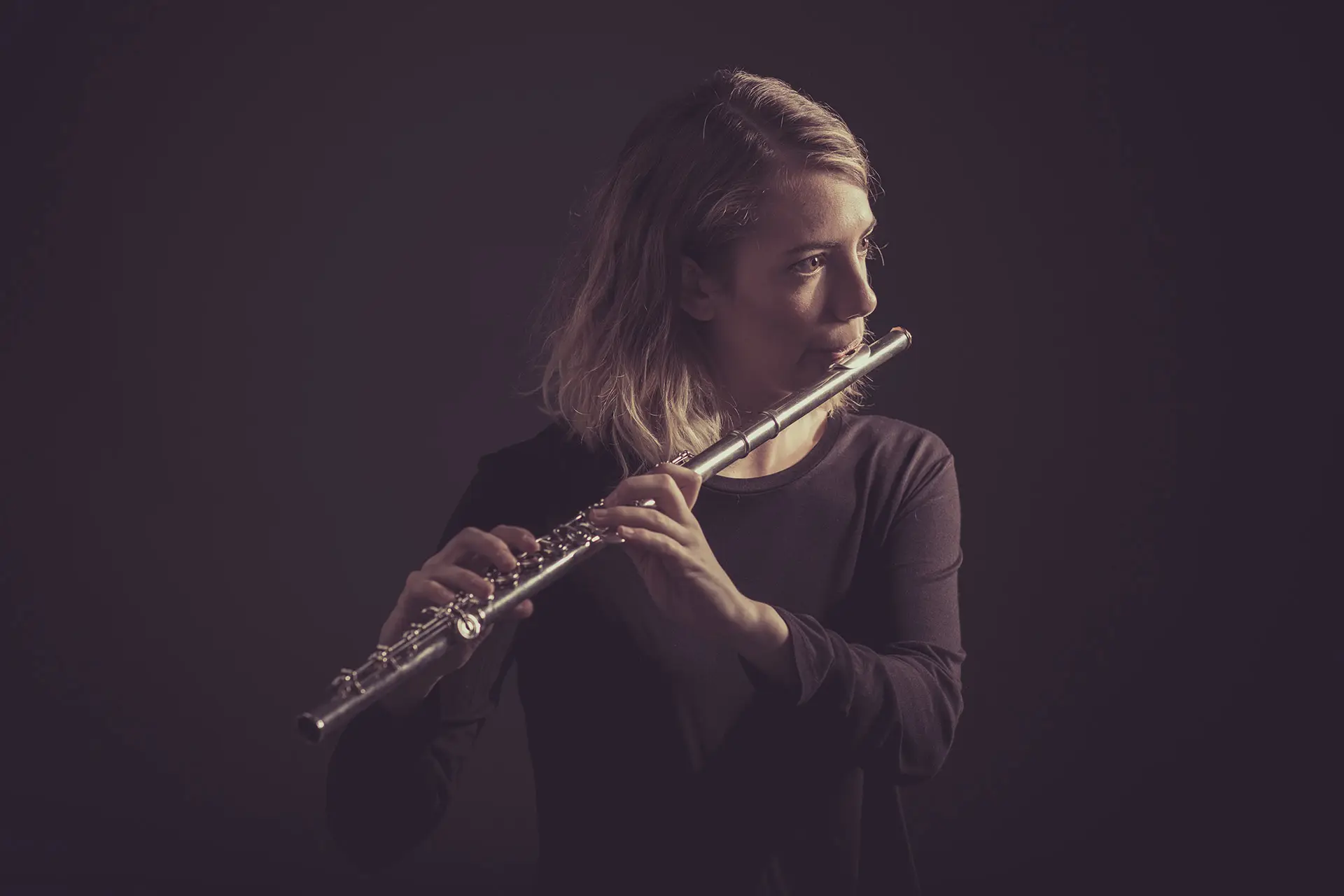 Woman playing a silver flute against a dark background