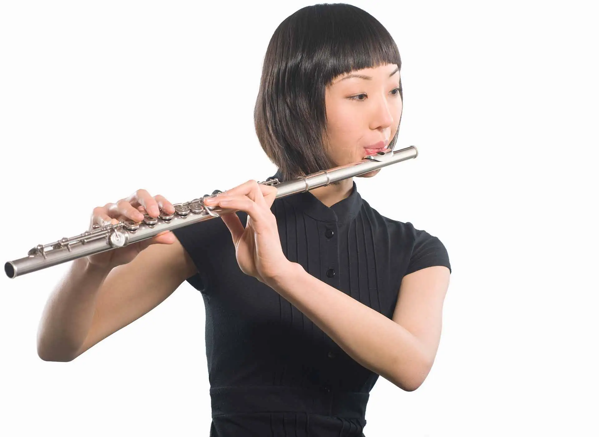 Woman playing a silver flute against a plain background