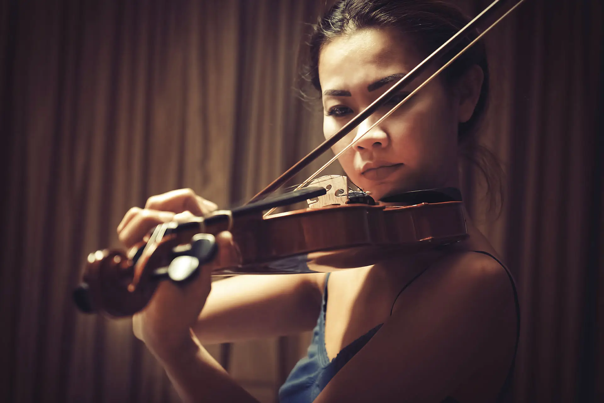 Woman playing violin in front of curtains