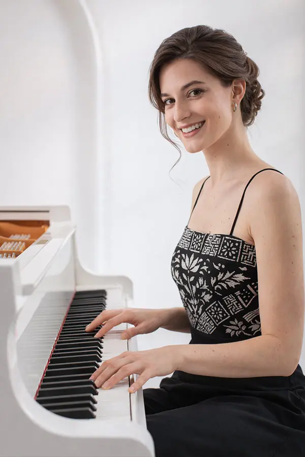 Smiling woman in a black dress playing a white piano