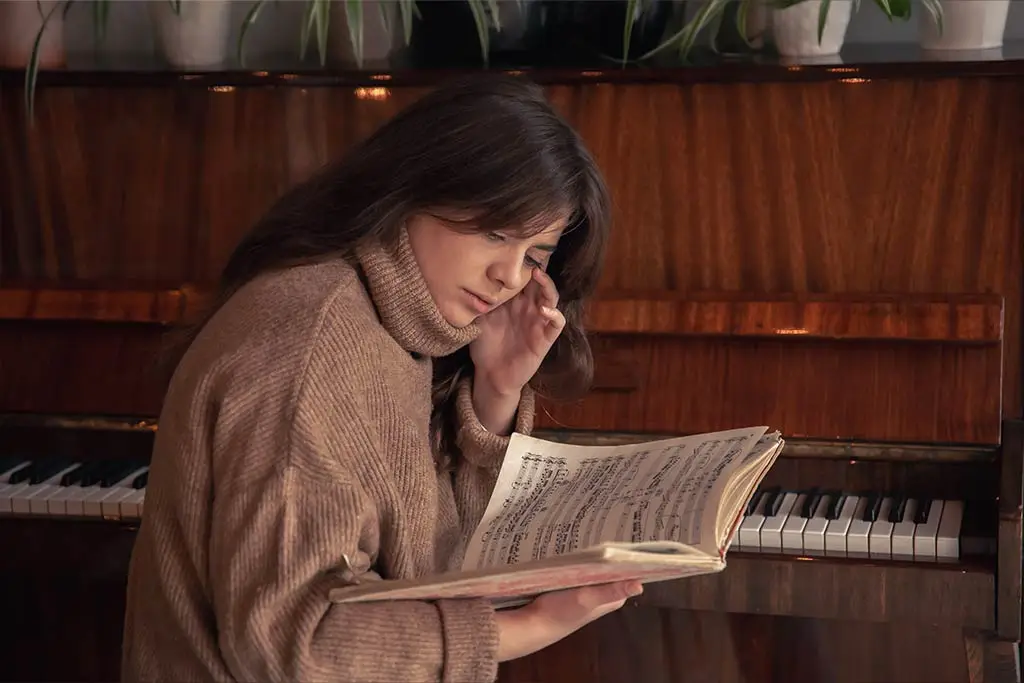 Woman reading sheet music beside an upright piano