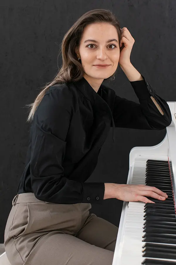 Woman seated at a piano with one hand on the keys