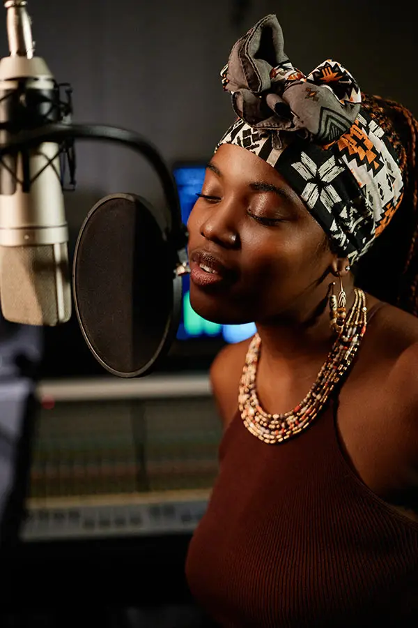 Woman in a headwrap singing into a studio microphone with pop filter