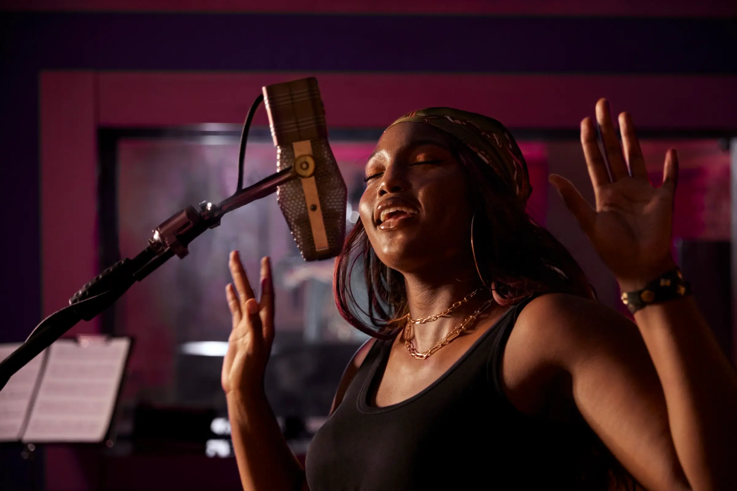 A woman singing into a studio microphone under pink light