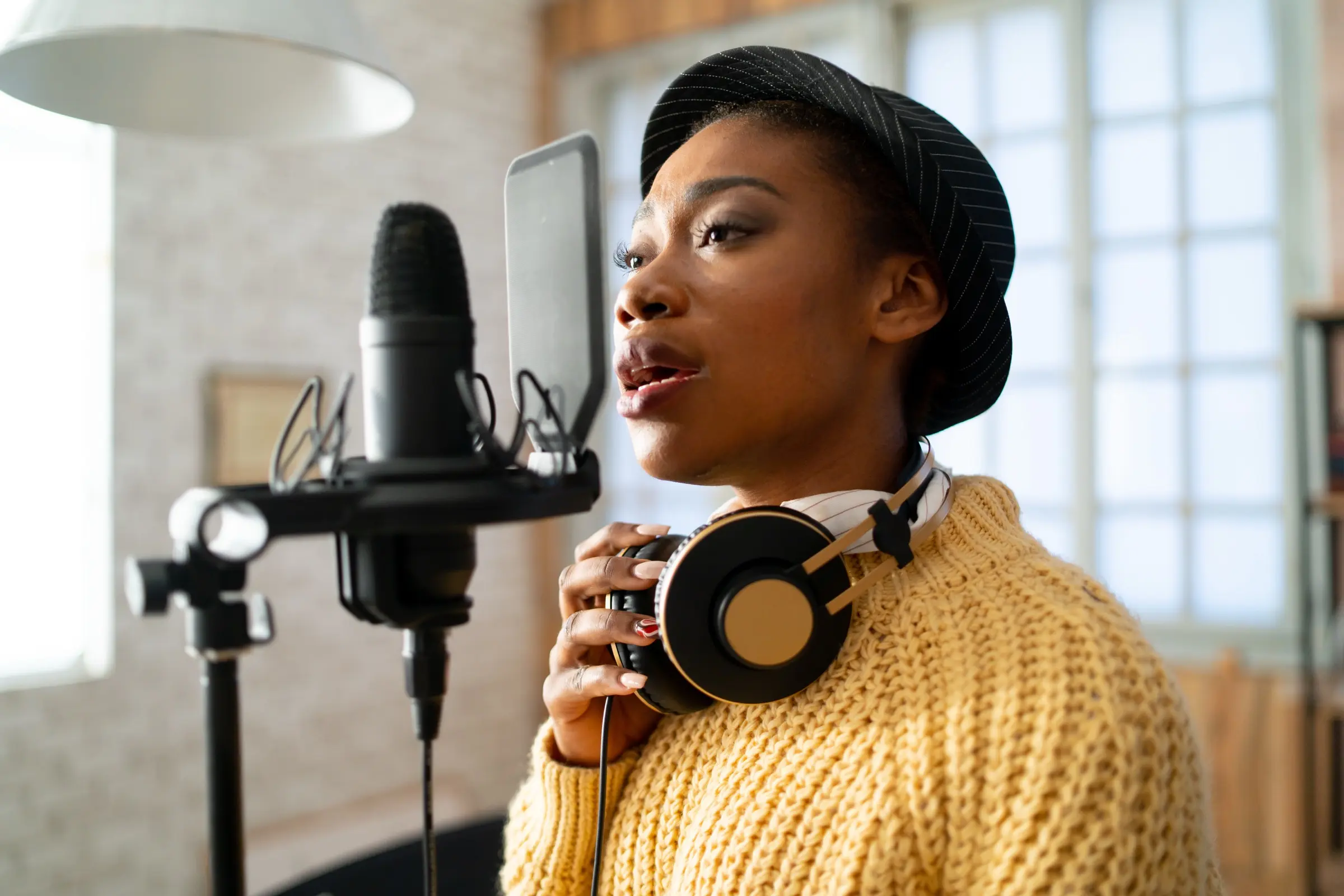 Woman singing into a studio microphone with headphones round her neck.