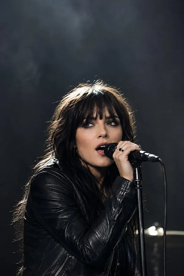 Woman in a leather jacket singing on a dark stage