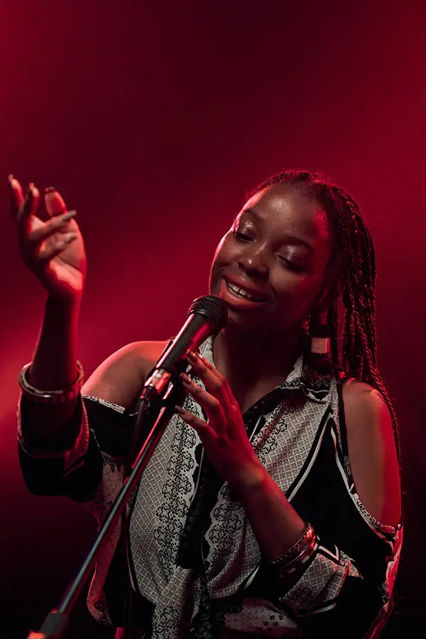 Woman singing into a microphone under red stage lighting