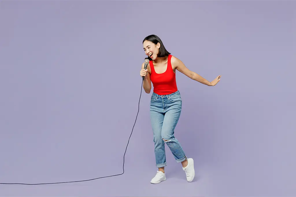 Young woman in a red top singing against a purple background