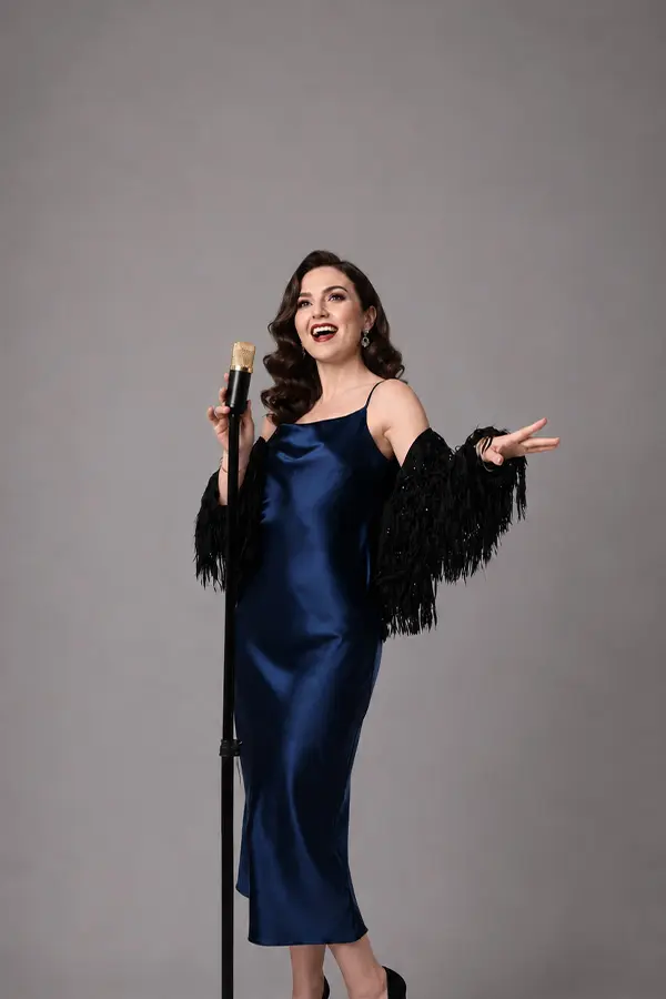 Woman in a blue satin dress singing at a vintage microphone