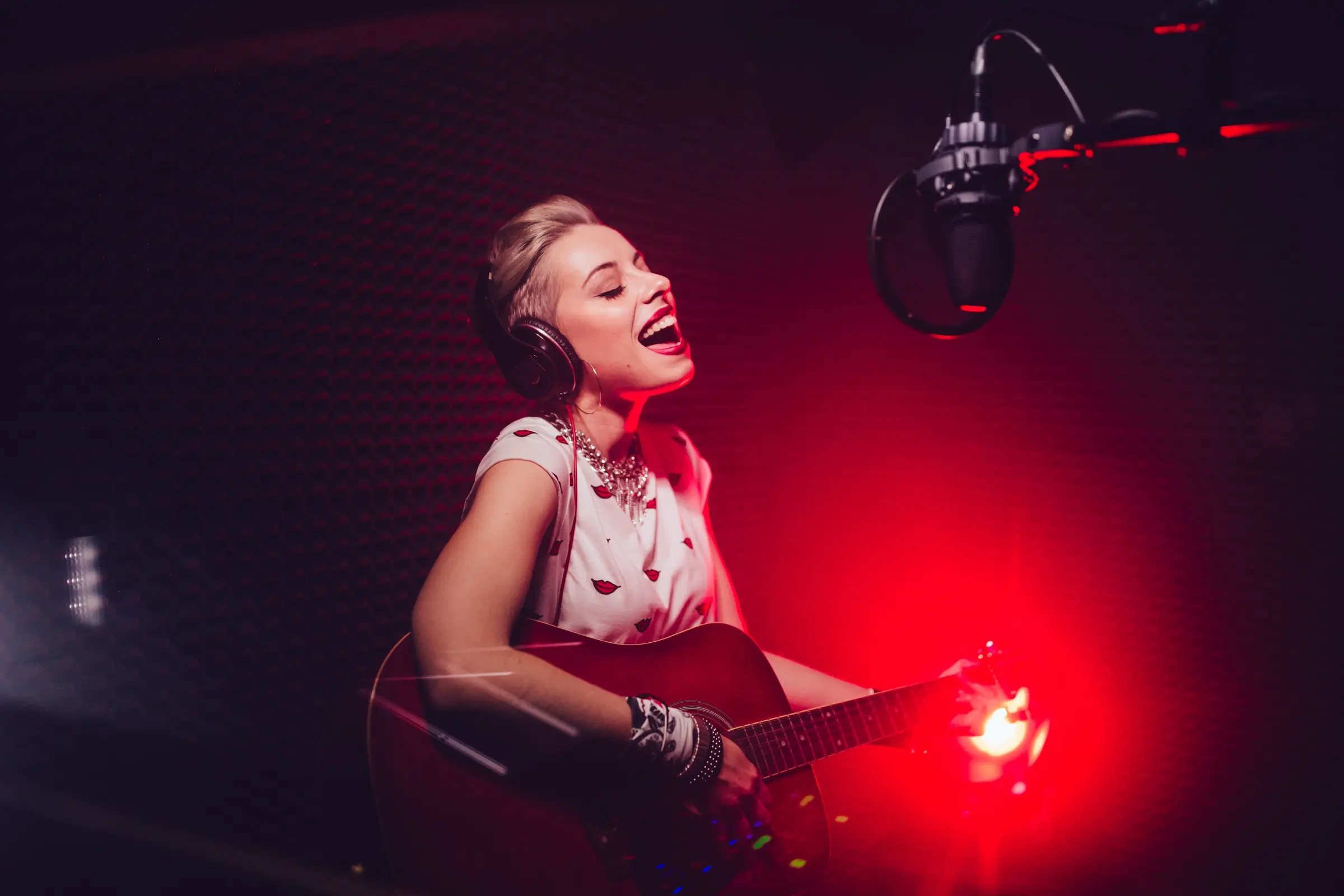 Singer playing guitar and singing into a microphone in a recording studio