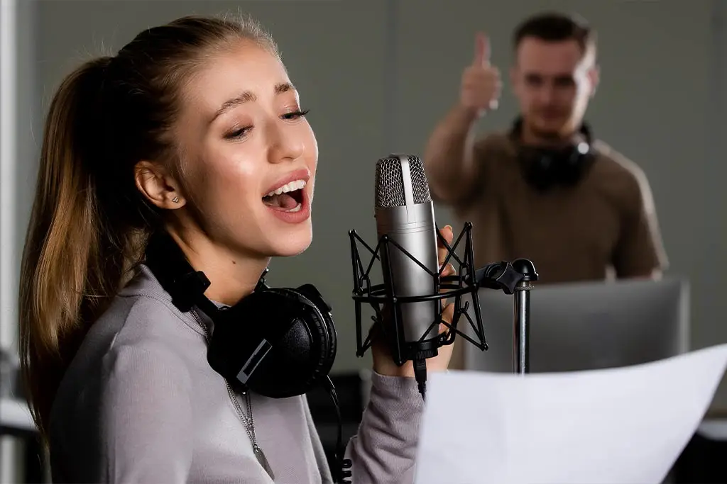 Woman singing into a studio microphone as a man gives a thumbs up