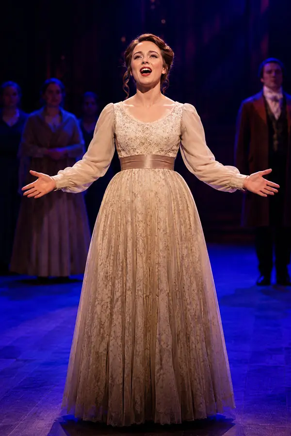 Woman singing on stage with an ensemble behind her