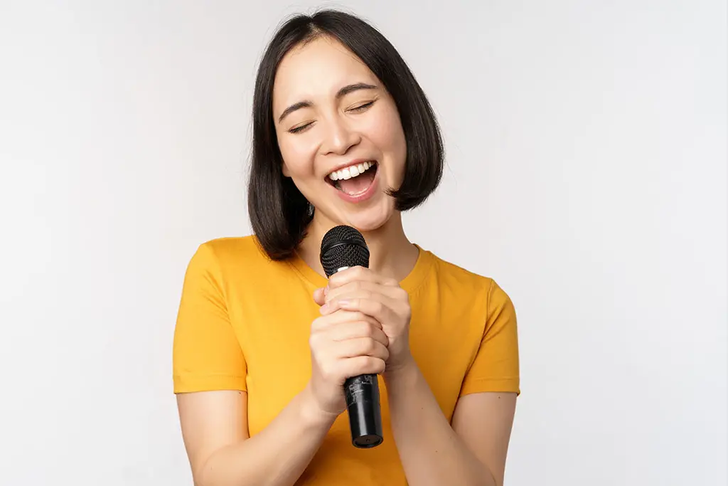 Woman in a yellow shirt singing with her eyes closed
