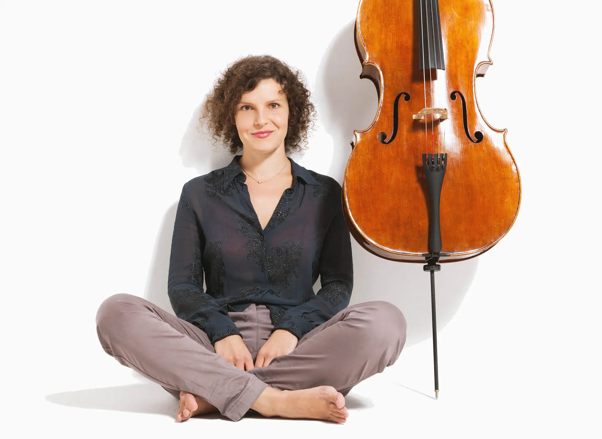 Woman sitting cross-legged beside a cello