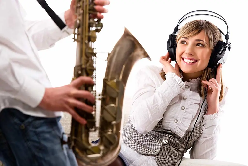 Woman wearing headphones beside a person holding a saxophone