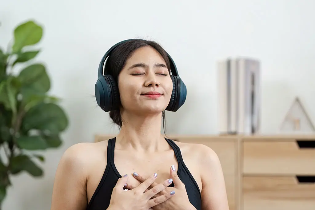 Woman wearing headphones with eyes closed and hands on chest