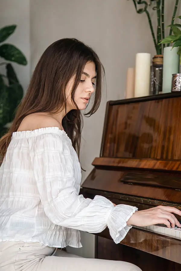 Woman in an off-shoulder white blouse playing an upright piano