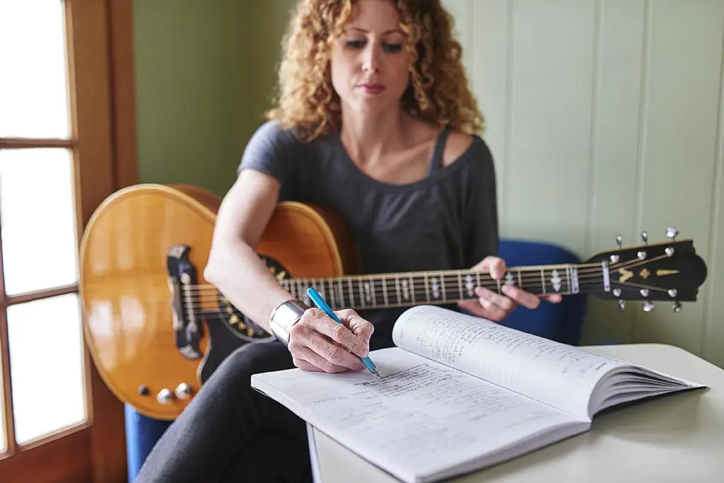 Woman writing in a notebook while holding an electric guitar