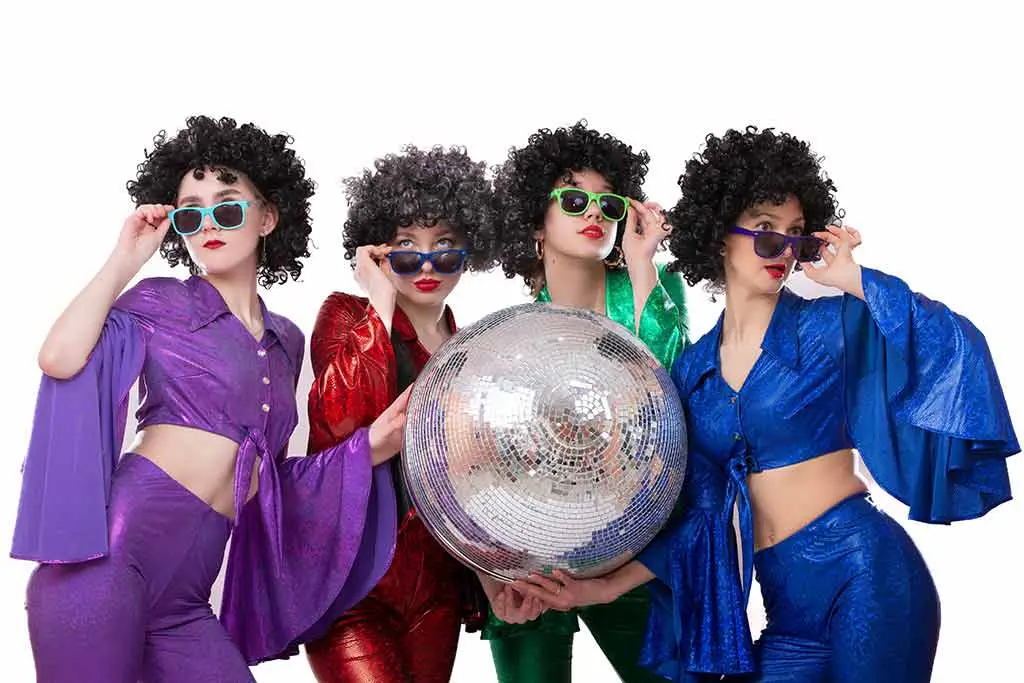 Four women in colourful disco outfits holding a mirror ball