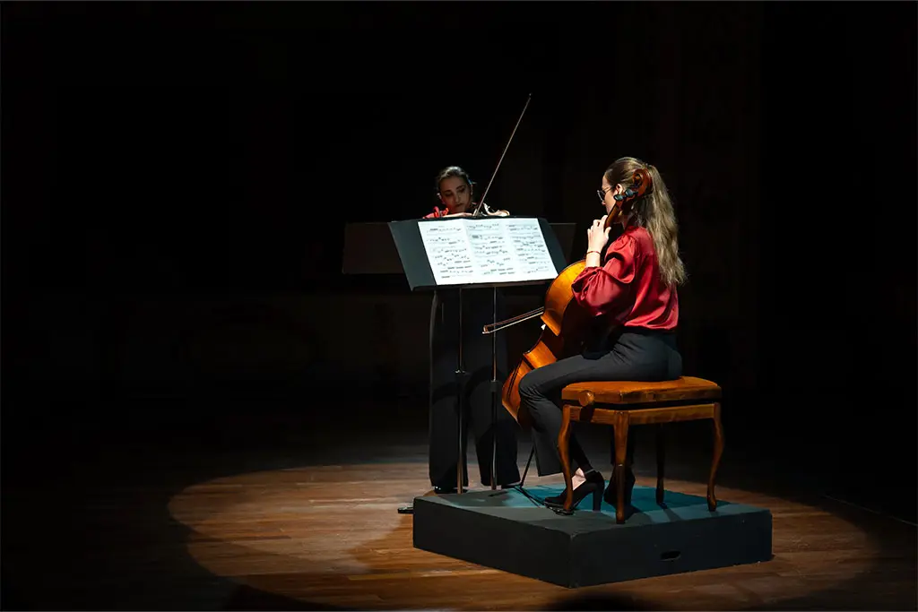 Two women playing cello and violin on a spotlighted stage