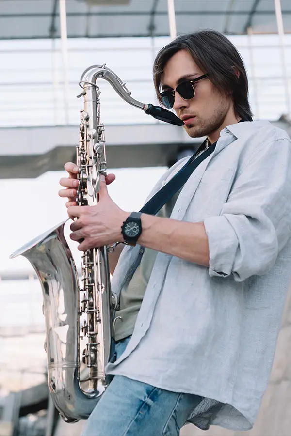Young man in sunglasses playing a baritone saxophone outdoors