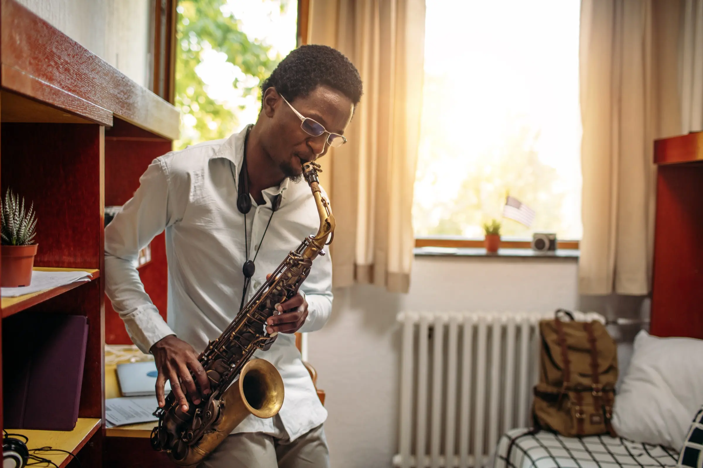 Young man practising the alto saxophone in a sunlit room.