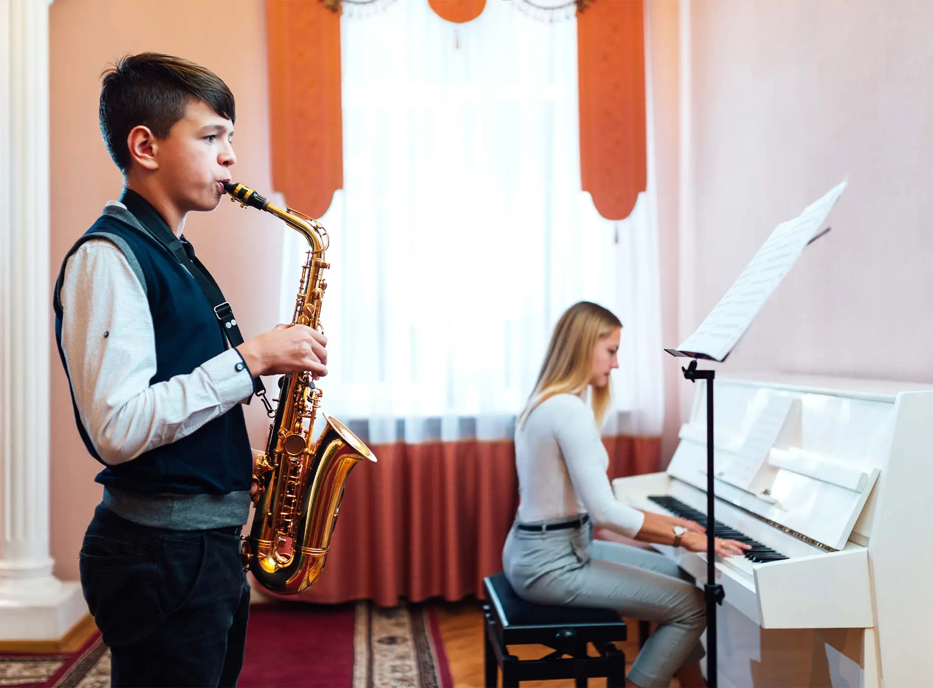 Young man practising saxophone with teacher playing piano