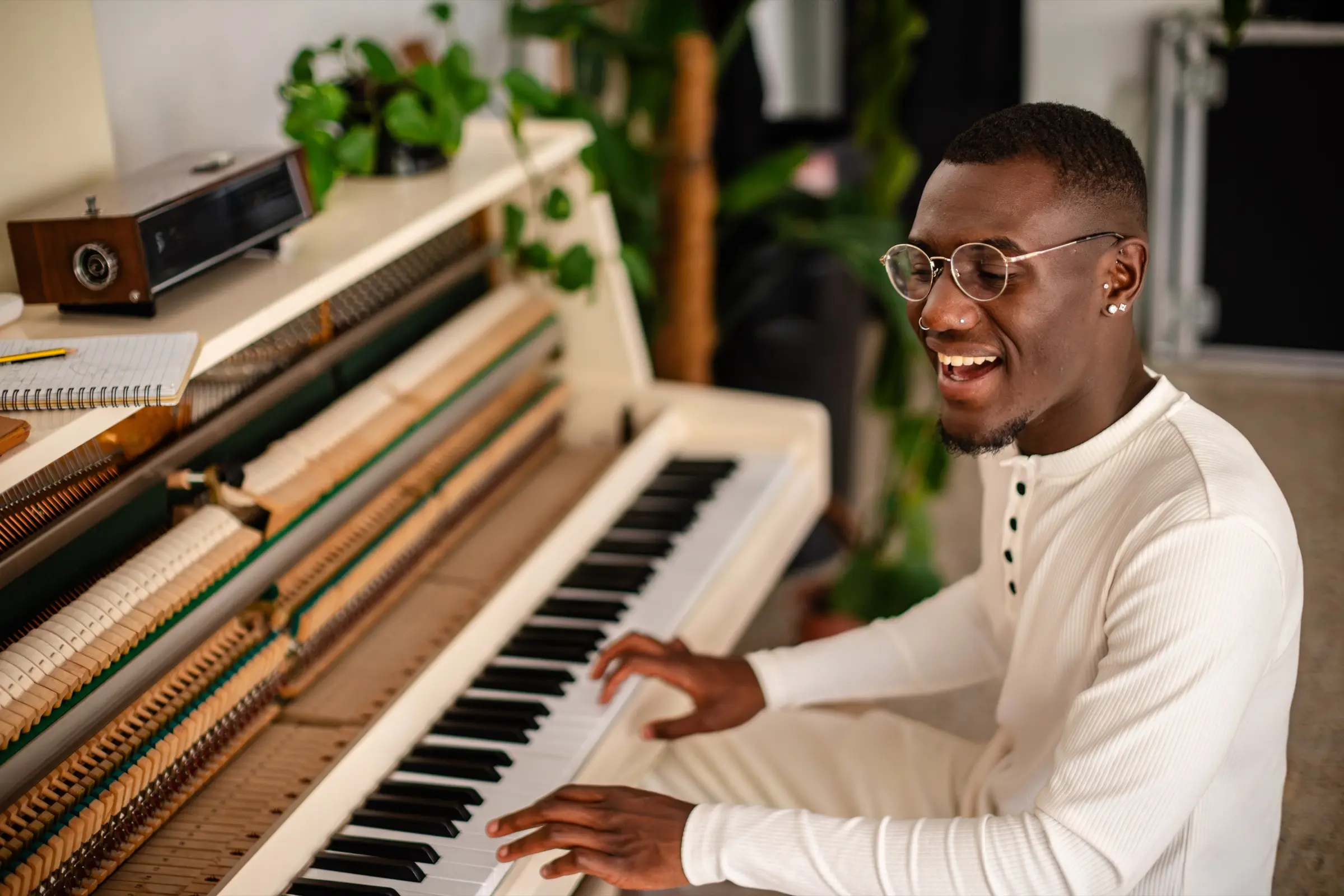 A young man smiling as he plays an upright piano in a bright studio
