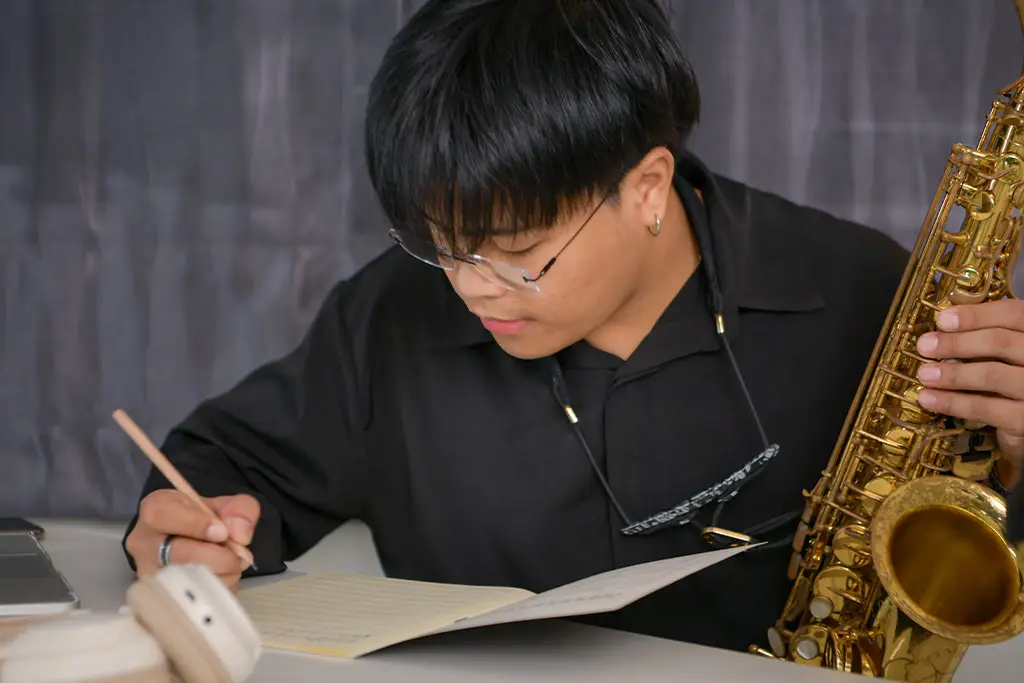 Young man writing in a notebook while holding a saxophone