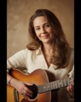 Smiling woman playing an acoustic guitar in a warm studio